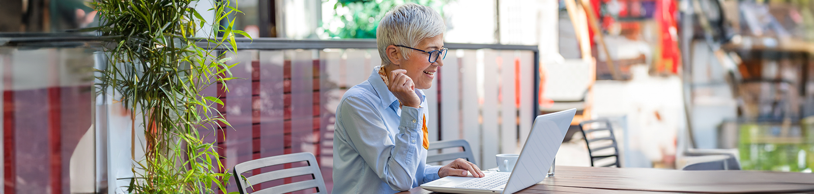 Smiling person sitting in sunny courtyard with an open laptop